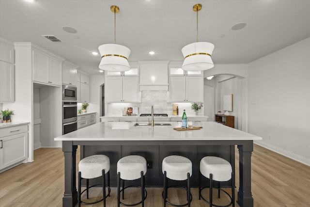 kitchen with arched walkways, stainless steel microwave, visible vents, and white cabinetry