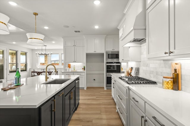 kitchen with visible vents, white cabinets, appliances with stainless steel finishes, premium range hood, and a sink