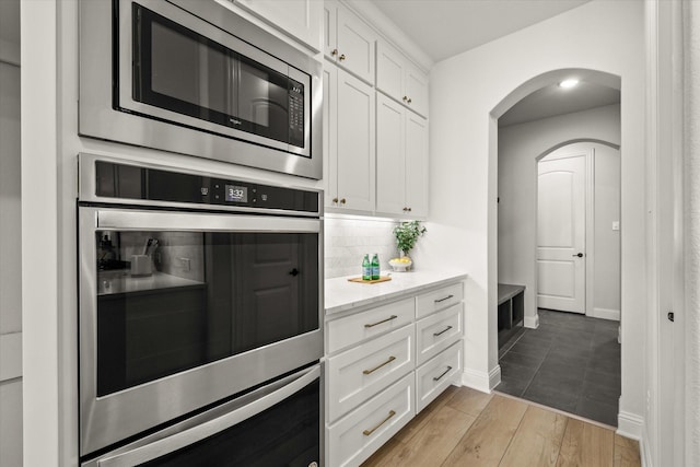 kitchen with arched walkways, stainless steel appliances, wood finished floors, white cabinetry, and tasteful backsplash