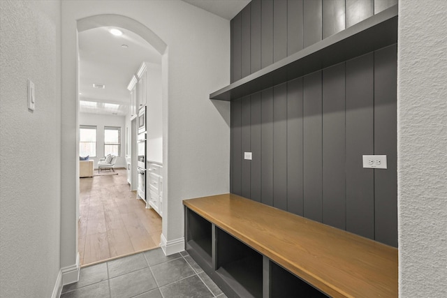 mudroom featuring a textured wall, baseboards, arched walkways, and dark tile patterned flooring