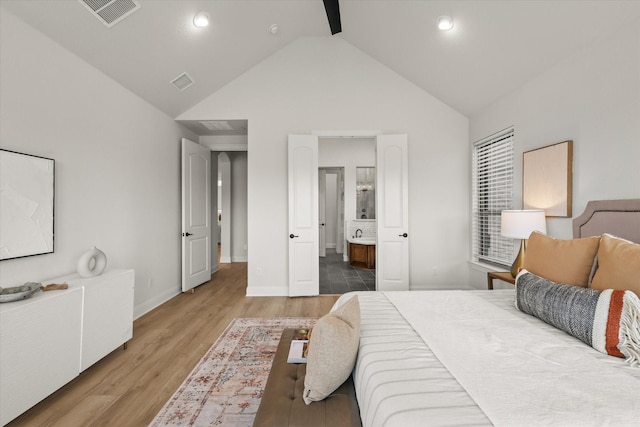 bedroom with high vaulted ceiling, ensuite bath, wood finished floors, and visible vents