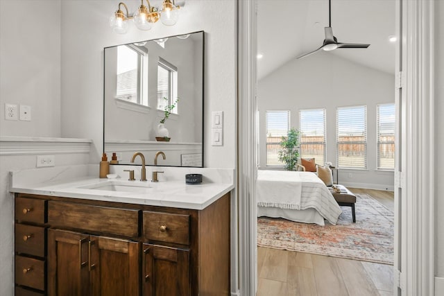 ensuite bathroom with vaulted ceiling, ceiling fan, vanity, wood finished floors, and baseboards