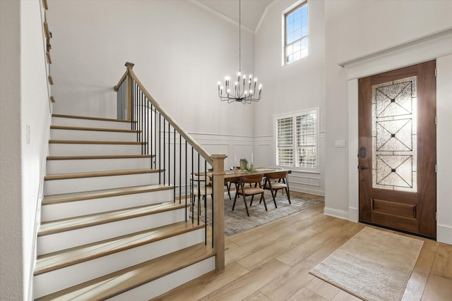 entryway with a chandelier, light wood-type flooring, a decorative wall, and stairway