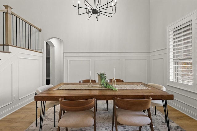 dining room with arched walkways, light wood-style floors, an inviting chandelier, and a decorative wall