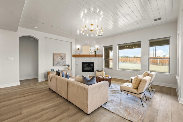 living room with arched walkways, a fireplace, light wood-style flooring, and baseboards