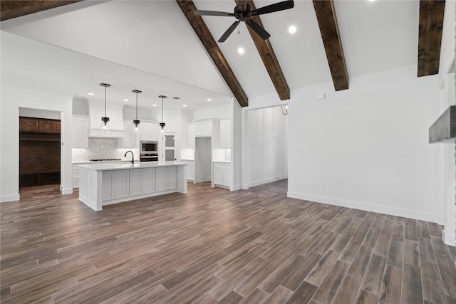 unfurnished living room featuring dark wood-type flooring, beam ceiling, a sink, and a ceiling fan