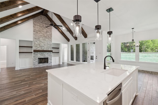 kitchen with white cabinets, a sink, wood tiled floor, a stone fireplace, and stainless steel dishwasher