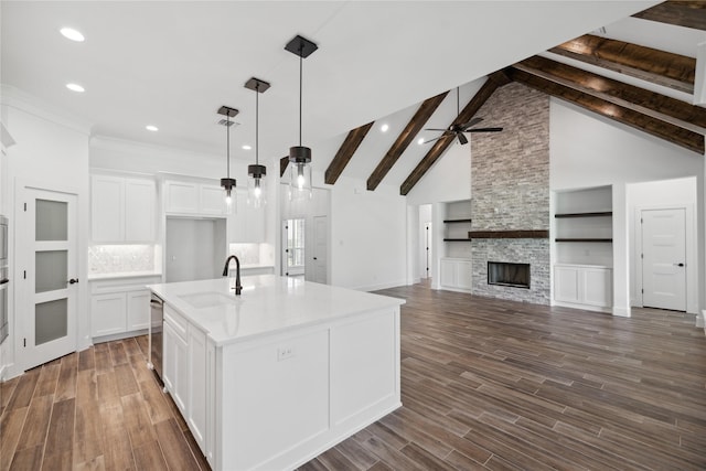 kitchen featuring dark wood-style flooring, a fireplace, a sink, stainless steel dishwasher, and beam ceiling