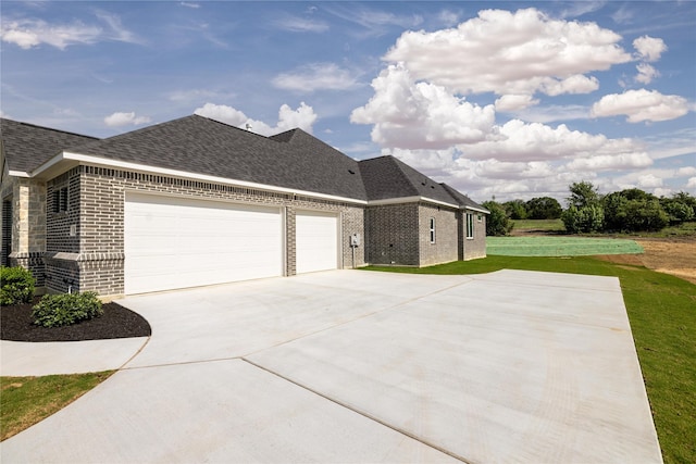 view of side of property featuring brick siding, a shingled roof, concrete driveway, a lawn, and a garage