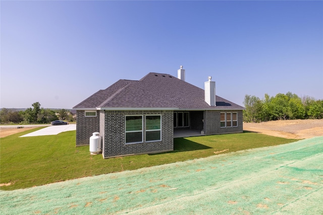 back of property featuring a patio, brick siding, a shingled roof, a yard, and a chimney