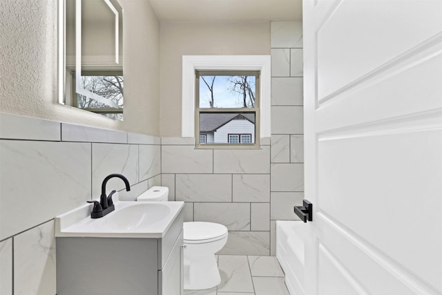 bathroom with toilet, marble finish floor, vanity, and tile walls