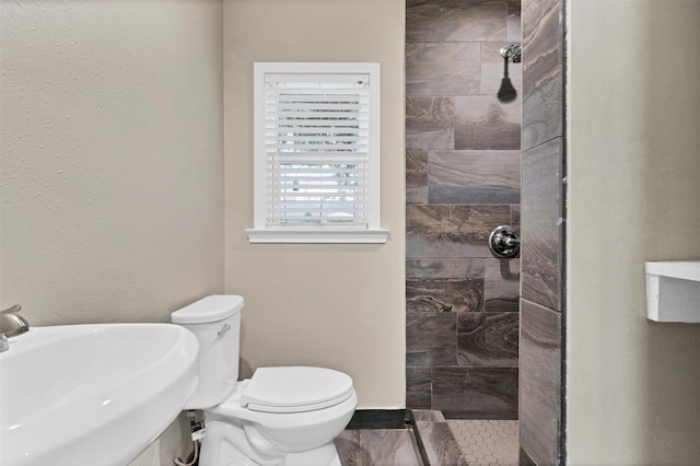 full bathroom with a tile shower, a sink, and toilet