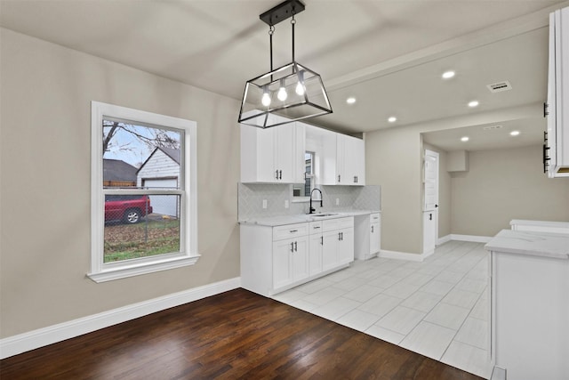 kitchen featuring tasteful backsplash, baseboards, visible vents, white cabinetry, and a sink