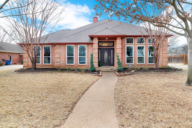 view of front facade featuring roof with shingles, brick siding, a chimney, and a front lawn