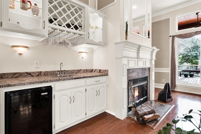 kitchen featuring wine cooler, glass insert cabinets, crown molding, a fireplace, and white cabinetry