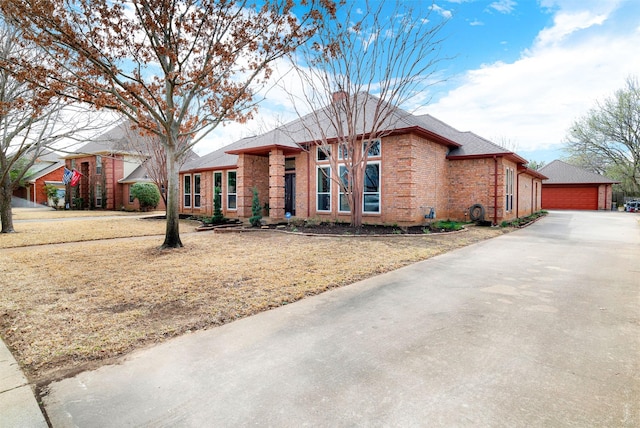 view of front of home featuring a garage, brick siding, an outdoor structure, and roof with shingles