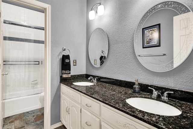 full bath featuring a textured wall, stone finish floor, a sink, and toilet