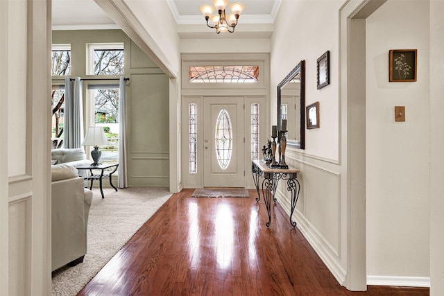 foyer entrance with crown molding, wood finished floors, a chandelier, and a decorative wall