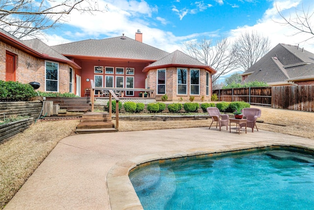 rear view of house with a fenced in pool, brick siding, a chimney, a patio area, and fence