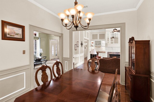 dining space featuring crown molding, a warm lit fireplace, a decorative wall, and wood finished floors