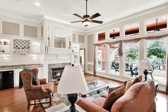 living area with light wood finished floors, ornamental molding, indoor wet bar, and a high end fireplace