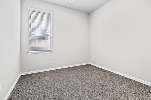 spare room featuring dark colored carpet, visible vents, and baseboards