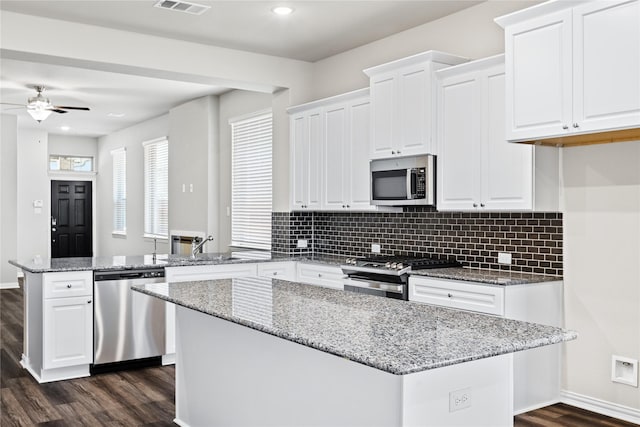 kitchen featuring white cabinets, appliances with stainless steel finishes, dark wood-style flooring, a center island, and a peninsula