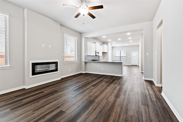 unfurnished living room with plenty of natural light, a glass covered fireplace, and dark wood finished floors