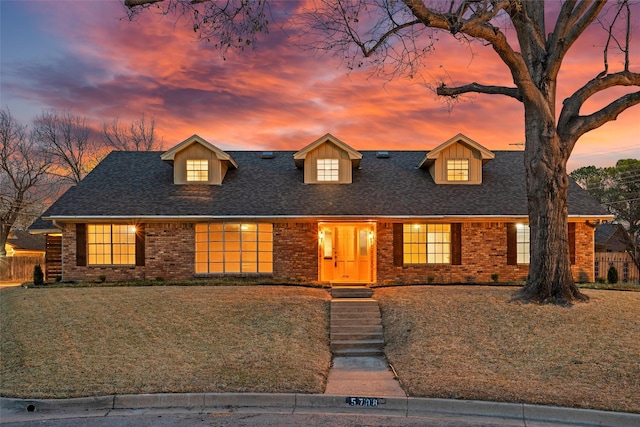 view of front facade featuring brick siding, a lawn, a shingled roof, and fence