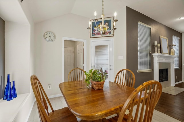 dining room with baseboards, a fireplace with flush hearth, vaulted ceiling, light wood-style floors, and a chandelier