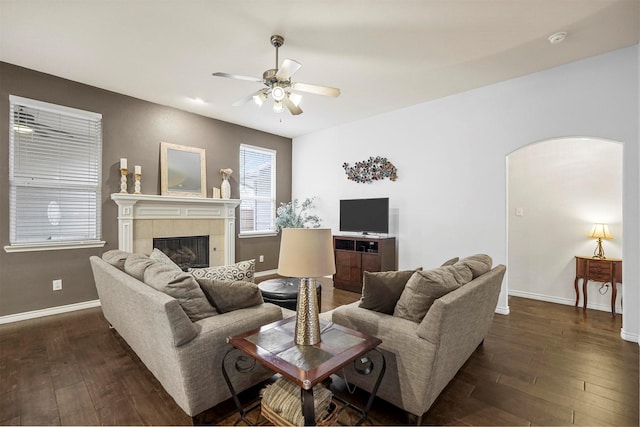 living area featuring baseboards, arched walkways, ceiling fan, dark wood-style flooring, and a fireplace