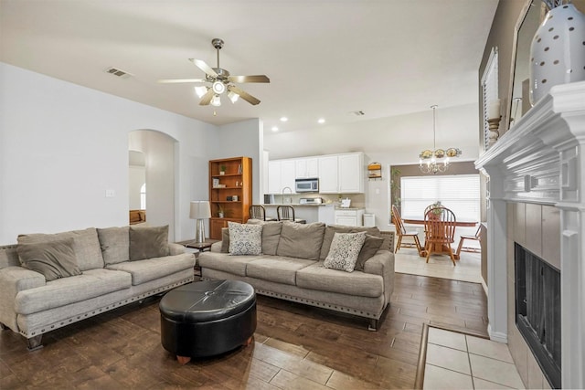 living room featuring arched walkways, ceiling fan with notable chandelier, a fireplace, visible vents, and light wood-type flooring