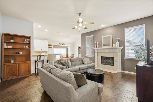 living room featuring ceiling fan, dark wood-style flooring, a fireplace, baseboards, and vaulted ceiling