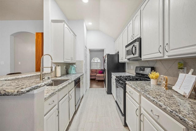 kitchen with appliances with stainless steel finishes, white cabinetry, vaulted ceiling, a sink, and light stone countertops