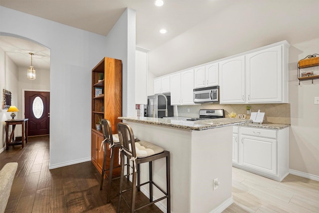 kitchen featuring decorative backsplash, appliances with stainless steel finishes, light wood-style floors, white cabinetry, and light stone countertops