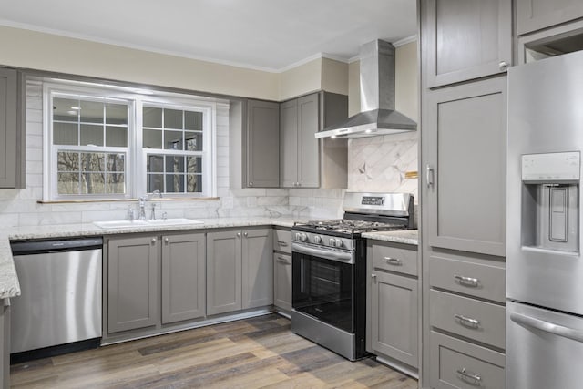 kitchen with crown molding, gray cabinets, appliances with stainless steel finishes, a sink, and wall chimney exhaust hood