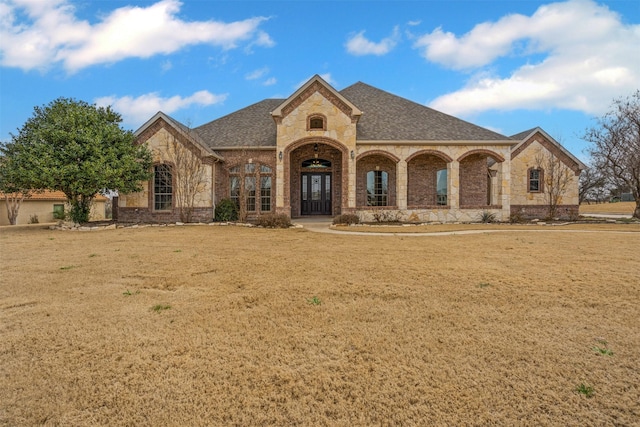 french country home with brick siding, a front lawn, and a shingled roof