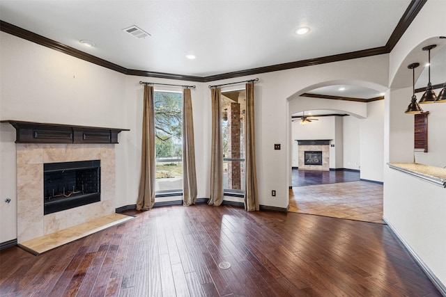 unfurnished living room featuring arched walkways, a fireplace, visible vents, wood finished floors, and baseboards