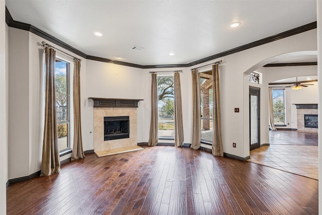 unfurnished living room featuring baseboards, visible vents, arched walkways, dark wood-style flooring, and a fireplace