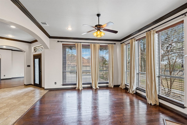 spare room featuring arched walkways, visible vents, ornamental molding, wood finished floors, and baseboards