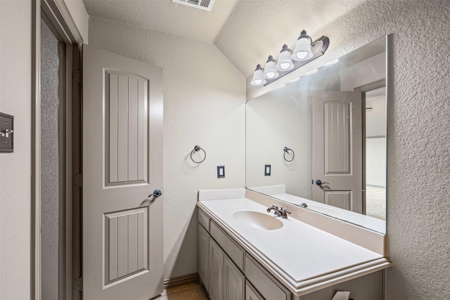 bathroom featuring visible vents, a textured wall, vaulted ceiling, vanity, and a textured ceiling