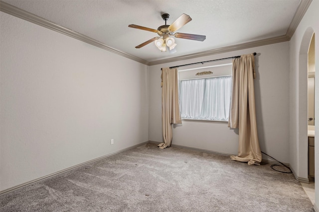 carpeted spare room with a textured ceiling, arched walkways, a ceiling fan, and ornamental molding