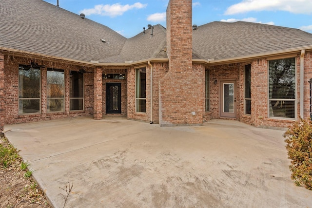 rear view of house with a patio area, a shingled roof, a chimney, and brick siding