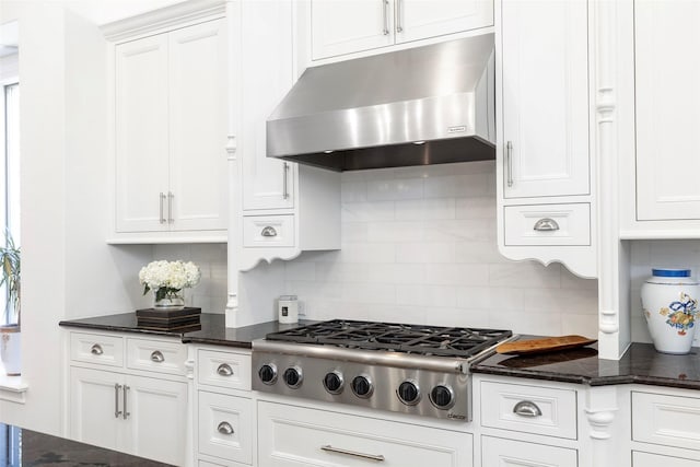 kitchen featuring tasteful backsplash, dark stone countertops, under cabinet range hood, stainless steel gas stovetop, and white cabinetry