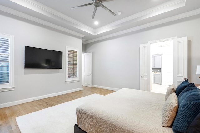 bedroom with light wood-type flooring, a raised ceiling, crown molding, and baseboards