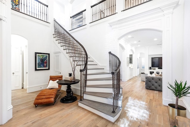 stairs featuring arched walkways, wood finished floors, a towering ceiling, baseboards, and a wealth of natural light