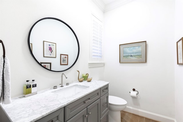 bathroom featuring baseboards, toilet, wood finished floors, crown molding, and vanity