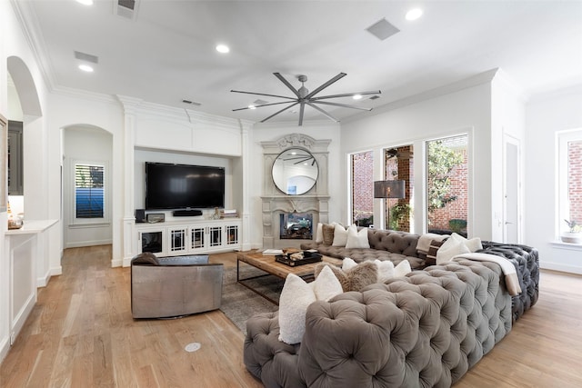 living area featuring ornamental molding, arched walkways, a large fireplace, and visible vents