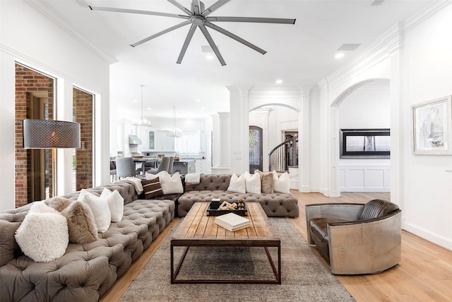 living area featuring arched walkways, light wood-style flooring, recessed lighting, baseboards, and crown molding