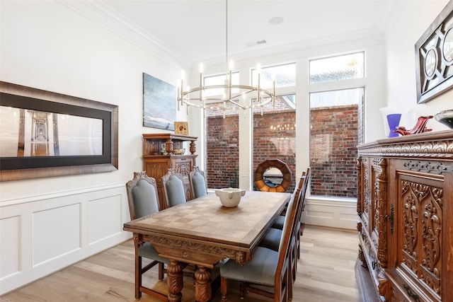 dining area with light wood-style floors, visible vents, ornamental molding, and a wainscoted wall